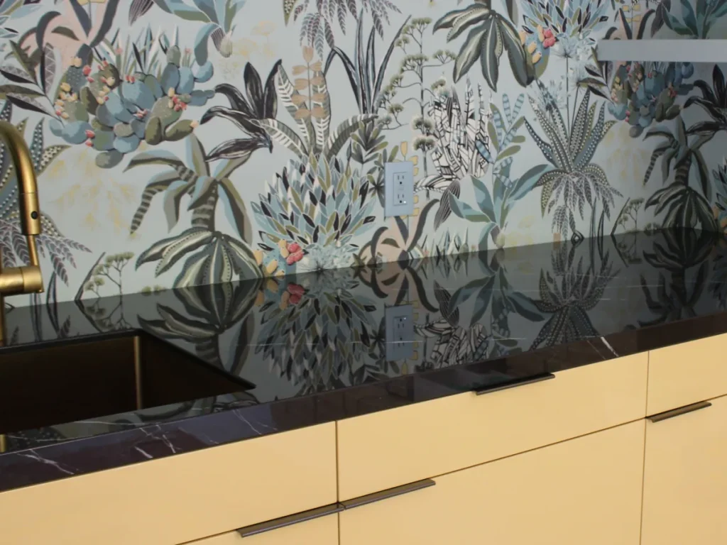 Black stone porcelain countertop in bathroom with gold sink, against floral print wallpaper